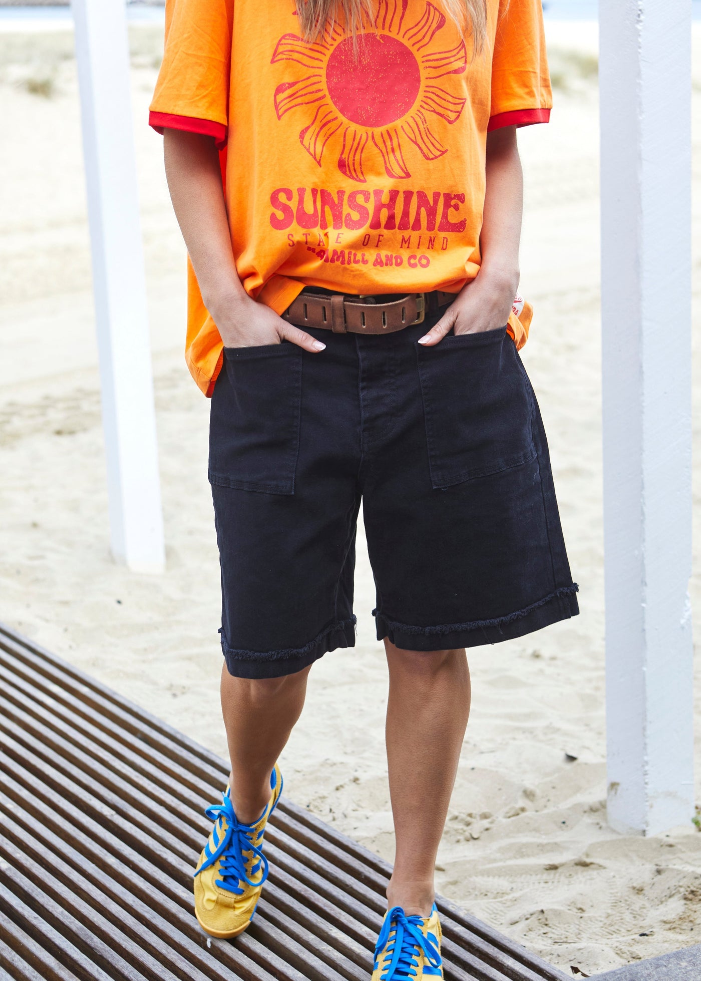 Hammill & Co pair of longer-length black stretch denim shorts with a relaxed fit. They have front pockets, a raw rolled hem, and sit mid-thigh